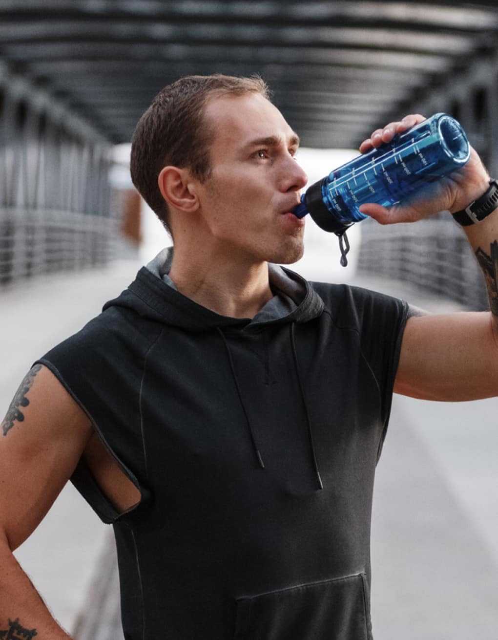 Man hydrating and drinking from a water bottle outside on bridge
