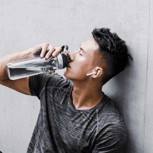 Dark haired man hydrating drinking from a water bottle against wall